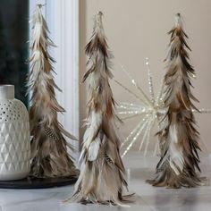 there are three fake trees in front of the mirror and one is white with brown feathers