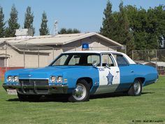 an old police car is parked on the grass in front of a house and fence