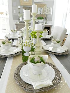 a dining room table set with white dishes and place settings, candlesticks and flowers