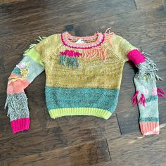 a colorful sweater with fringes on it laying on the floor next to a pair of scissors