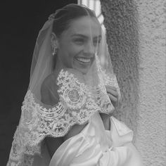 a woman in a wedding dress and veil smiles at the camera while standing next to a wall