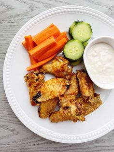 a white plate topped with chicken wings, carrots and cucumbers next to ranch dressing