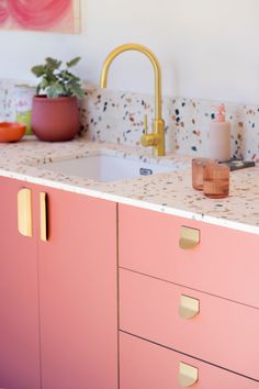 a kitchen with pink cabinets and marble counter tops, gold faucets and potted plants