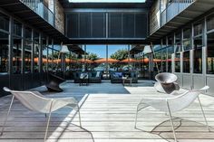 two white chairs sitting on top of a wooden floor next to tall glass walls and windows