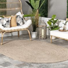 a living room with two wicker chairs and a round rug on the floor next to potted plants