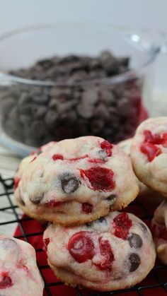 cookies with chocolate chips and cherries are cooling on a rack in front of a bowl