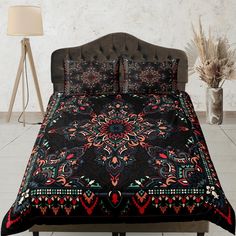 a bed covered in a black and red comforter next to a vase with flowers