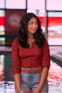 a woman in overalls and a red cardigan is standing by the pool with her hands in her pockets