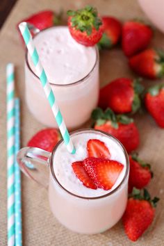 two glasses filled with milk and strawberries on top of a table next to some strawberries