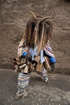 a person with long hair and horns on their head is walking down the street in front of a building