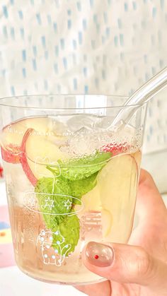 a person holding up a glass filled with ice and apple slices on top of it