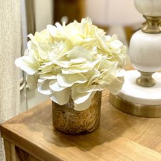 a vase filled with white flowers sitting on top of a wooden table next to a lamp