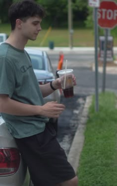 a young man sitting on the back of a white car holding a cup of coffee