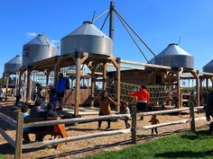 several people are playing on a wooden play structure with large metal tanks in the background