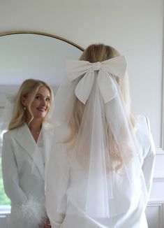 a woman wearing a white veil and standing next to another woman in front of a mirror