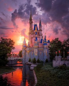 the castle is lit up at sunset with clouds in the sky and trees around it