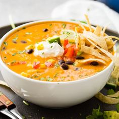 a bowl of mexican soup with tortilla chips and sour cream on the side