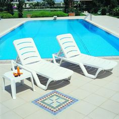 two lawn chairs sitting next to a swimming pool with a rug on the ground near it