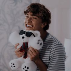 a young man holding a white teddy bear in his hands and smiling at the camera