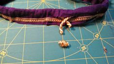 a pair of gold chains on top of a purple cloth next to scissors and thread