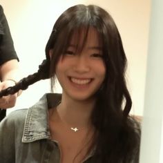 a woman with long hair is smiling and getting her hair styled by another person in the background