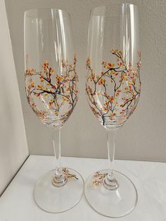 two wine glasses sitting on top of a white table next to each other with orange and yellow flowers painted on them