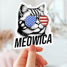 a hand holding up a sticker with a cat wearing sunglasses and the word meowca