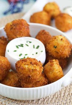 some fried food in a white bowl with a small dip on the side and green sprinkles