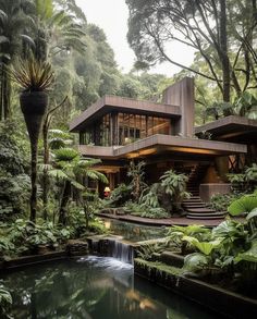 the house is surrounded by lush green trees and plants, with a waterfall running through it