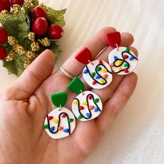 a person is holding three colorful earrings in their hand next to some berries and holly