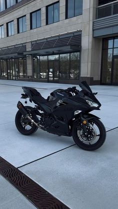 a black motorcycle is parked in front of a large building with glass doors and windows