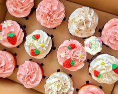 a box filled with lots of pink cupcakes covered in frosting and topped with strawberries