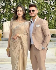 two people standing next to each other in front of a flower covered wall with white flowers