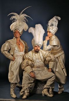 three men dressed in fancy costumes posing for the camera with feathers on their head and shoulders