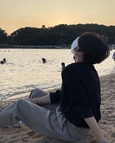 a person sitting on the beach with their feet in the sand and people swimming in the water behind them