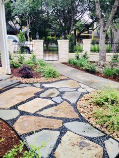 a stone walkway in front of a house with trees and bushes around it, leading to a gate