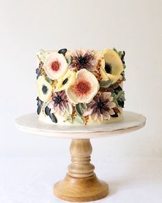 there is a cake with flowers on it sitting on a stand in front of a white wall