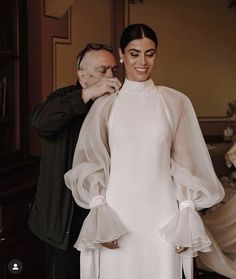 a man and woman standing next to each other in front of a white wedding dress