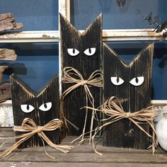 three black cat faces are tied to wooden blocks with twine and pumpkins in the background