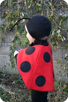 a child wearing a ladybug costume standing in front of a brick wall with ivy growing on it