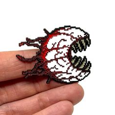 a hand holding a small red and white brooch