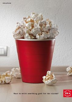 a red bucket filled with popcorn sitting on top of a wooden table next to a light switch