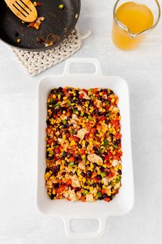 a casserole dish filled with rice and vegetables next to a glass of orange juice