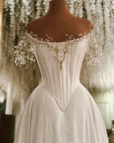 a white wedding dress on display in front of a mirror with flowers hanging from it