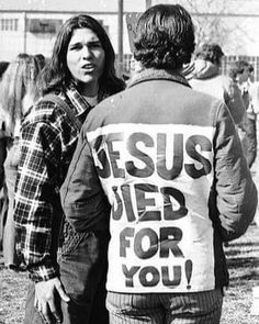 black and white photograph of two people standing in front of a building with a sign that says jesus wed for you