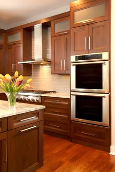 a kitchen with wooden cabinets and stainless steel ovens, wood flooring and marble counter tops