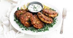 a white plate topped with chicken patties next to a bowl of ranch dressing and a fork