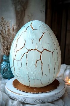 a cracked egg sitting on top of a white plate next to a blue vase and candles