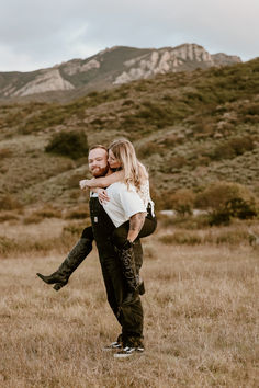 a man carrying a woman on his back in a field with mountains in the background