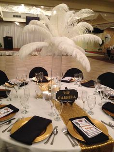 the table is set with black and gold place settings, silverware, and white centerpieces